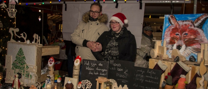 Op de Kerstmarkt Westervoort is ook een marktkraam waar houten producten verkocht worden. Twee kraamhouders achter de kraam. Kerst, markt, kramen, kerstsfeer, kerstverlichting. 
